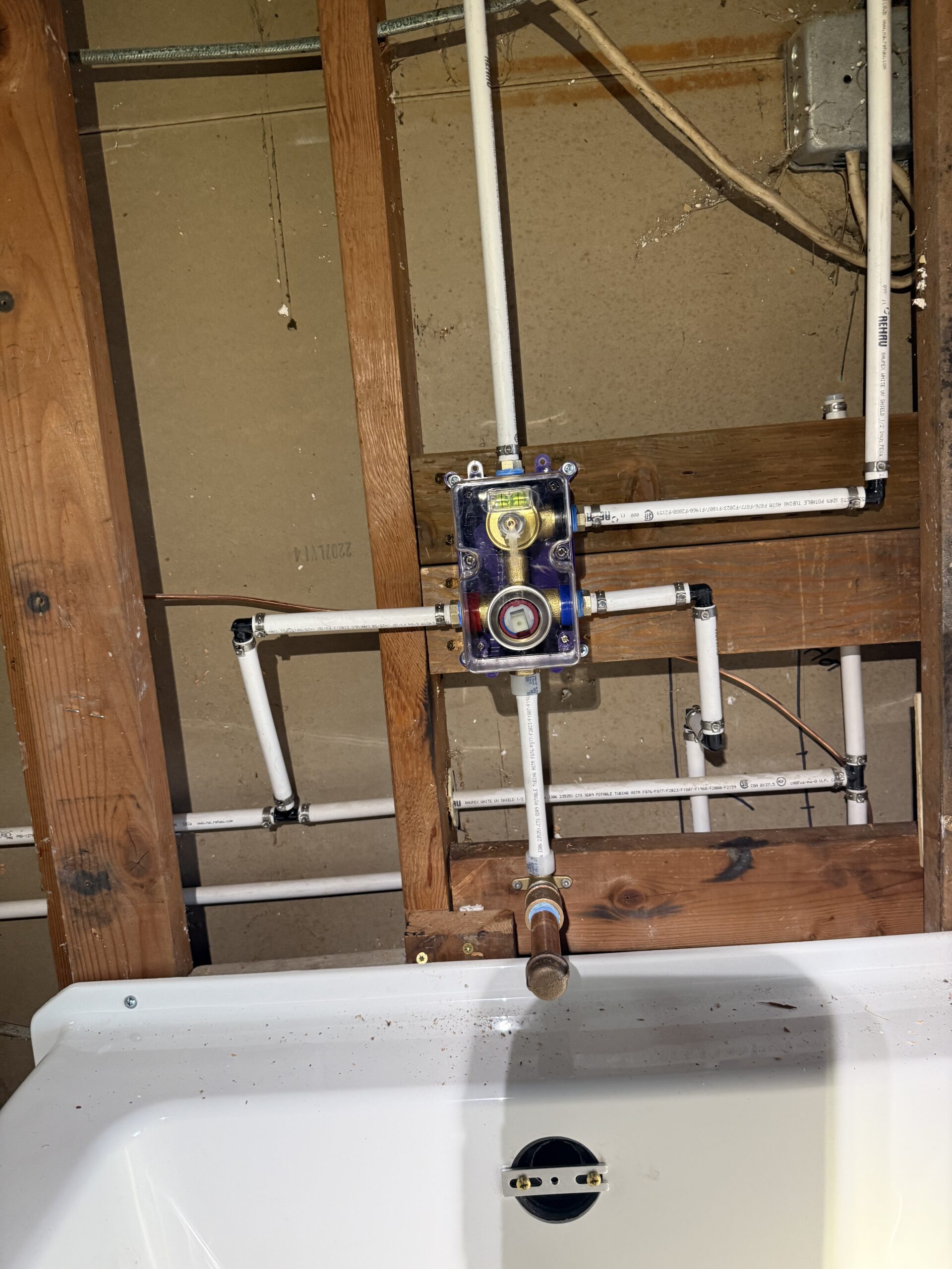 About Us: Exposed PVC plumbing and pipes are installed in a wooden wall frame above a white sink, with a valve and wiring visible.